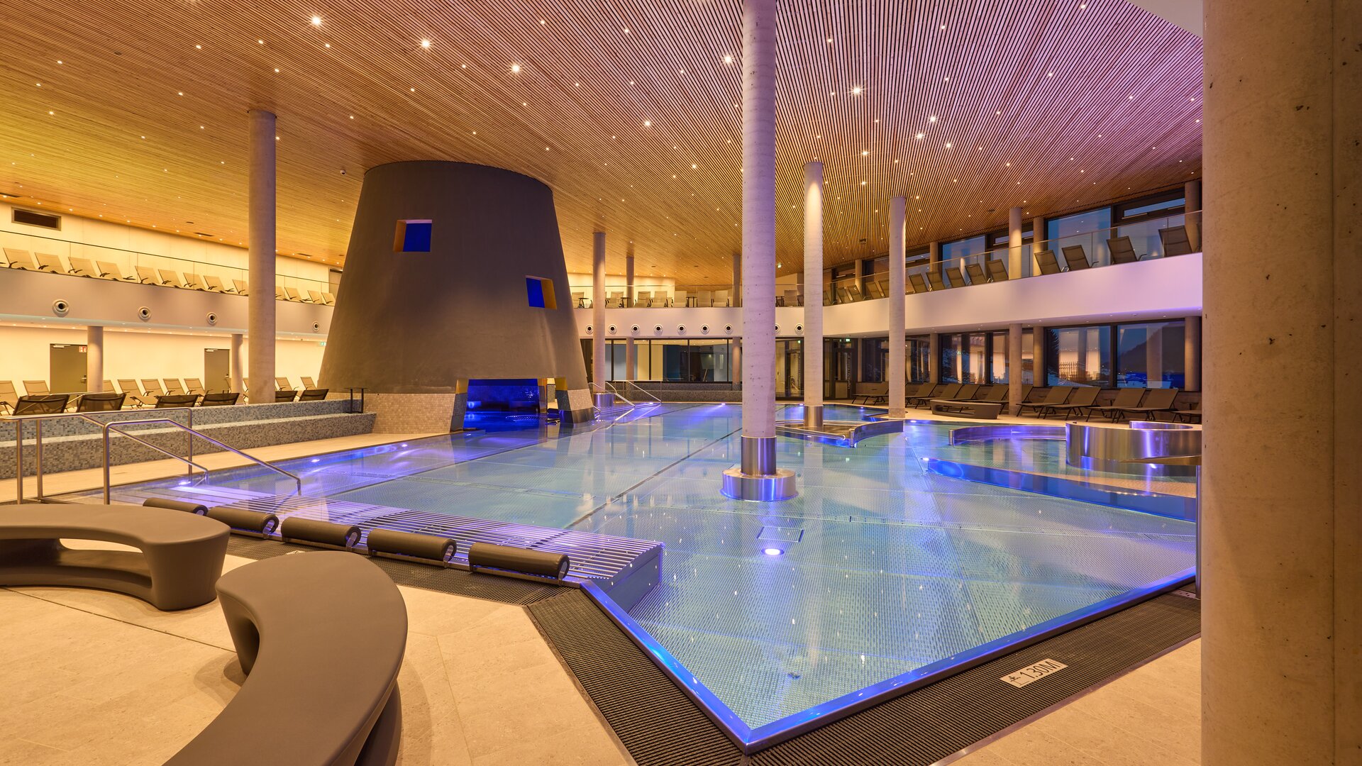 Moderner Innenpool mit blauer Beleuchtung, Holzdecke und Liegen
