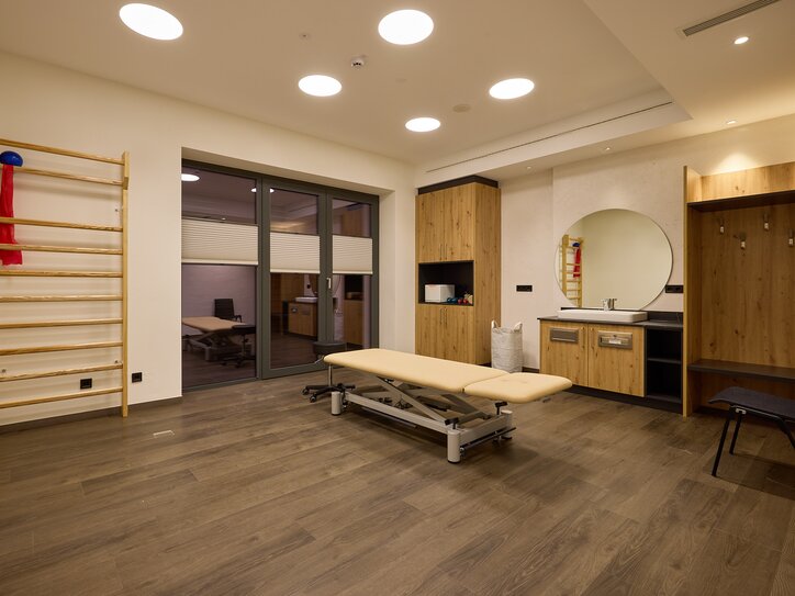 Physiotherapieraum mit Behandlungsliege, Sprossenwand und Holzmöbeln