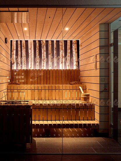 Sauna with warm lighting, wooden paneling and bucket for infusions