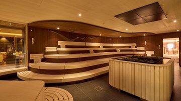 Innenbereich der Sauna mit halbkreisförmigen Holzbänken und zentralem Ofen