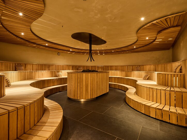 Round sauna with wooden benches on multiple levels and a heating element in the center