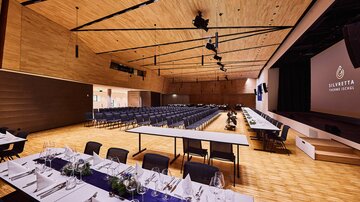 Großer Veranstaltungssaal mit Bühne, Leinwand und gedeckten Tischen, vorbereitet für Event in der Silvretta Therme