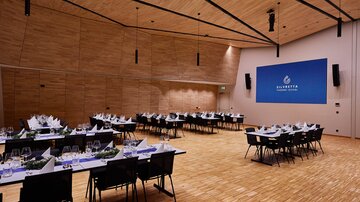 Großer Veranstaltungssaal mit gedeckten Tischen, Holzdecke und Leinwand