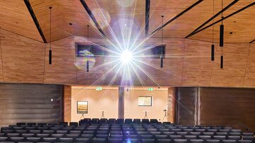 Veranstaltungssaal mit schwarzen Stuhlreihen, Holzdecke und zentralem Lichtstrahl