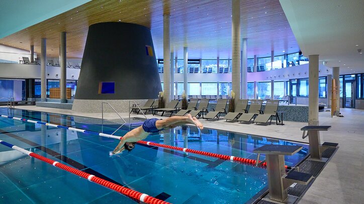 Ein Schwimmer springt mit einem Köpfler ins Sportbecken