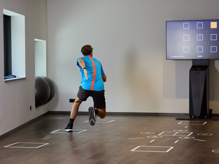 Man training in fitness studio using a screen, floor markings visible