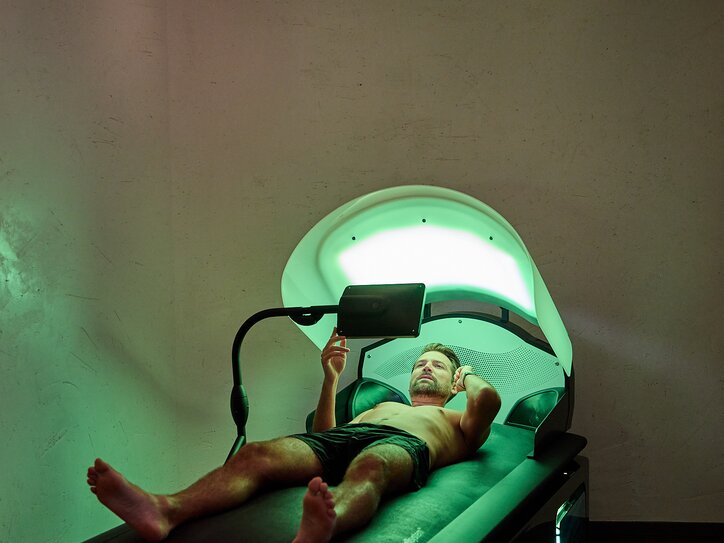 A man is receiving a water massage on a Wellys lounger while looking at a screen