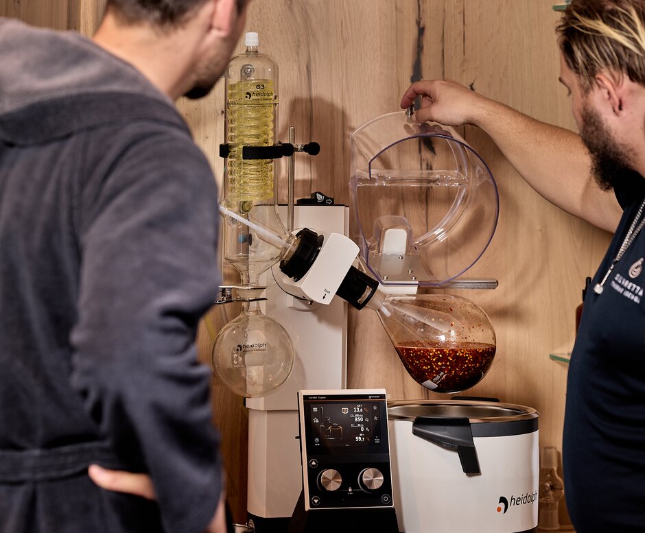 A man shows two guests an aroma device with glass parts and buttons