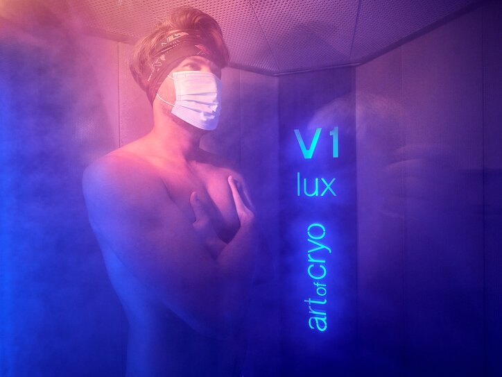 Cold chamber with blue lighting, dense mist and person undergoing cryotherapy treatment